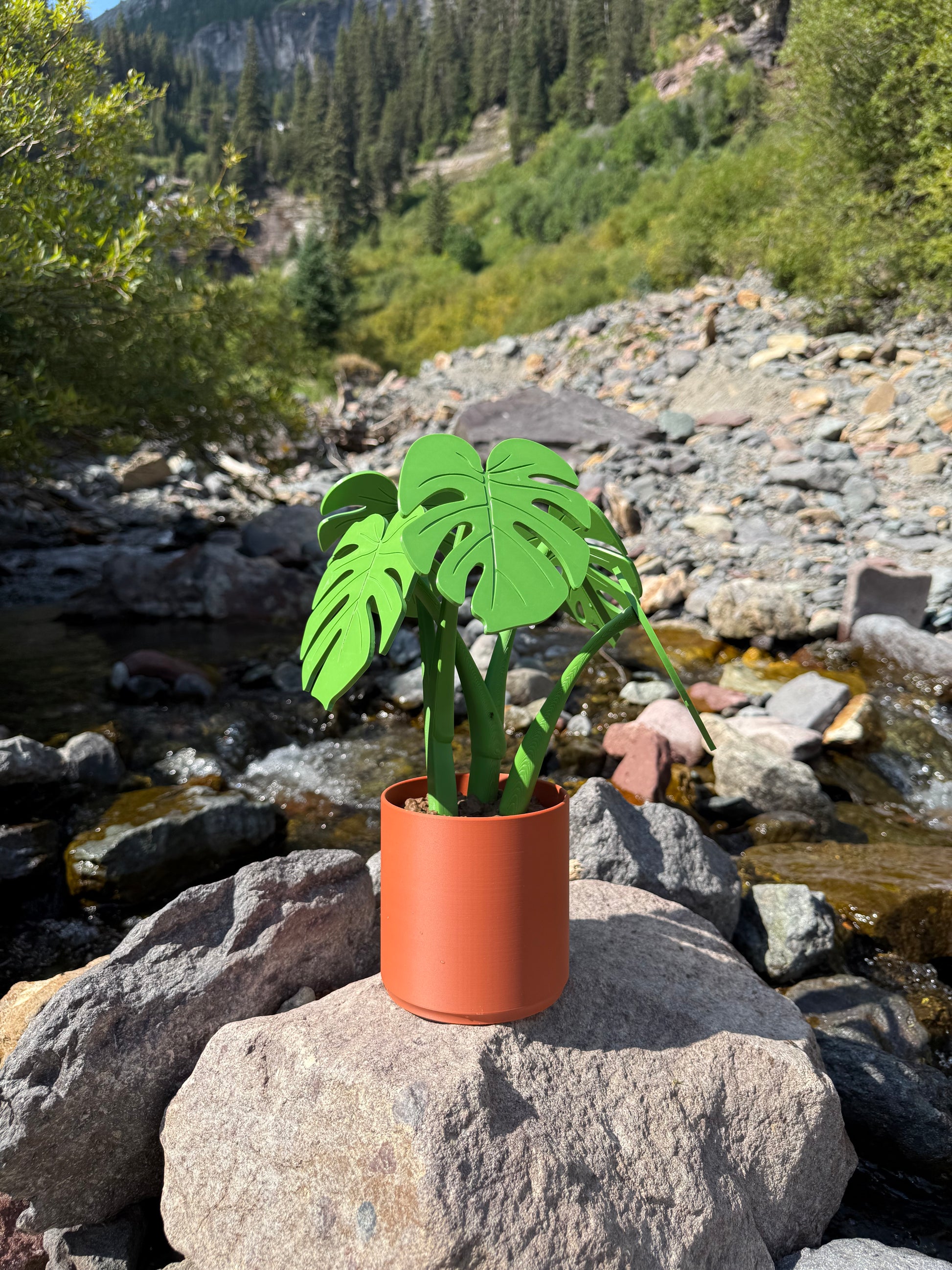 Artificial plant with green leaves and a terracotta pot on a rocky surface