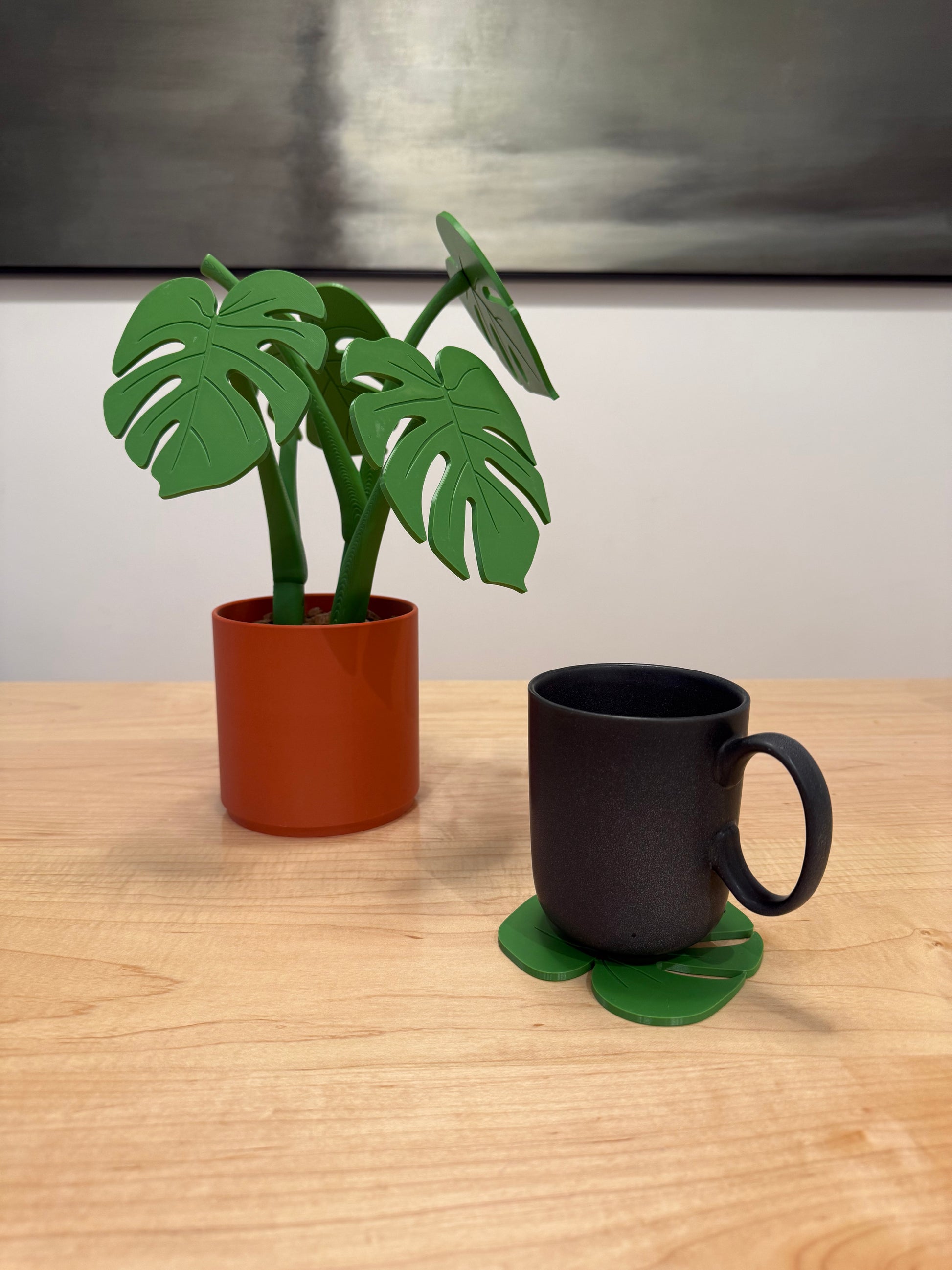 Black mug on leaf coaster and brown pot with green leaf decorations on a wooden surface.